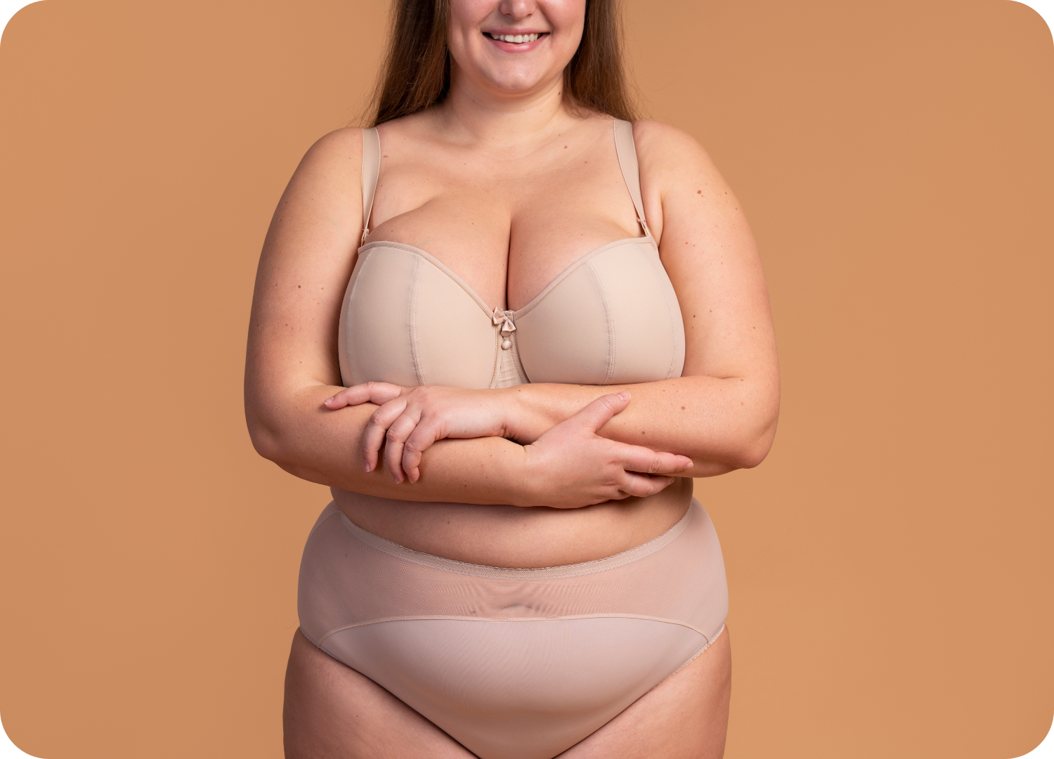 Mulher sorrindo com seios grandes, característicos da gigantomastia, vestindo lingerie de sustentação na cor nude.